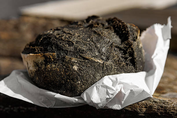 A close-up shot of a crusty, dark-baked round loaf of bread resting on crumpled parchment paper in natural sunlight.
