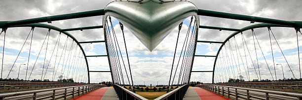or a wide-angle shot of an iron bridge with visible construction or rope elements, set in an urban environment, with a blurred background and a two-lane road. urban bridge wide angle.