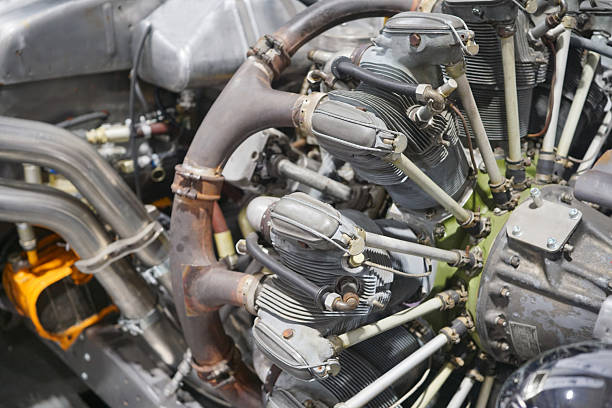 This black and white photograph captures the intricate mechanical details of a motorcycle engine's side profile. The image is filled with industrial components, prominently featuring the ribbed cooling fins of the cylinder head, a bolted engine casing, and a network of rubber hoses secured with metal clamps. Textural details, such as the braided sheathing on the wiring and the varying sheen of the metal surfaces, are emphasized by the high-contrast lighting, highlighting the rugged construction of the vehicle's powertrain.