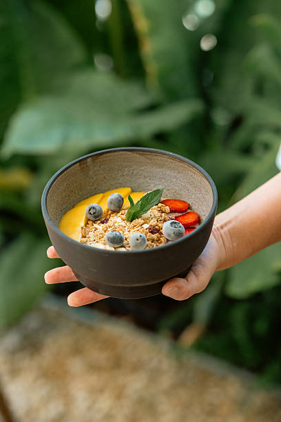 Healthy breakfast bowl with granola, fruits, and berries held by hand outdoors