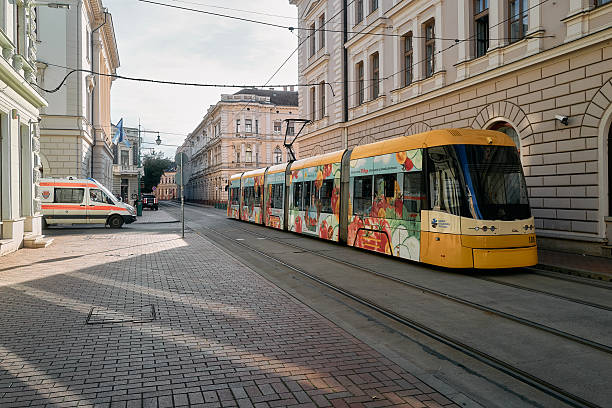 A yellow tram is on a track in front of a building. The train is decorated with a colorful design. Szeged, Hungary, 8 October 2024.