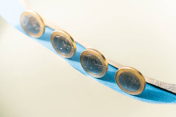 Multiple euro coins arranged along a crack in pastel background, representing fragile savings, inflation pressure and economic imbalance.