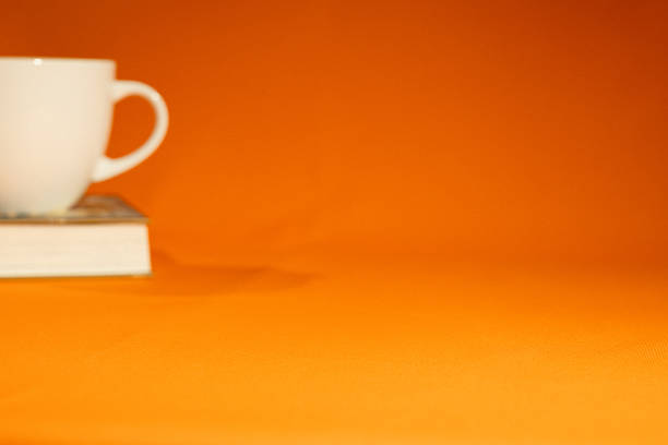 minimal workspace with coffee cup and book on orange background