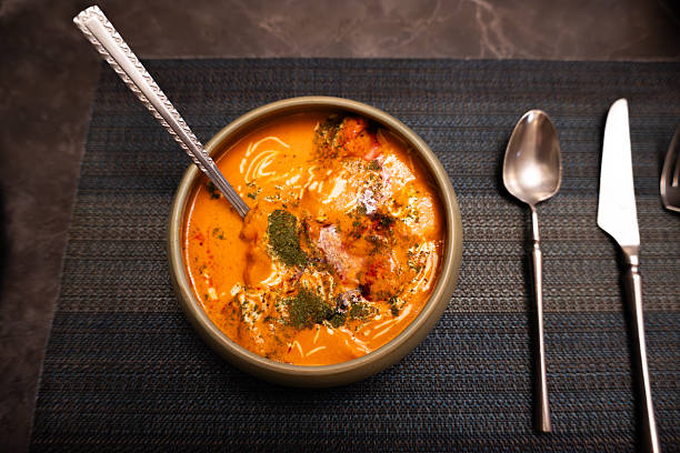 Indian Butter Chicken Curry in ceramic bowl with spoon, garnished with herbs and cream, served on textured placemat with cutlery