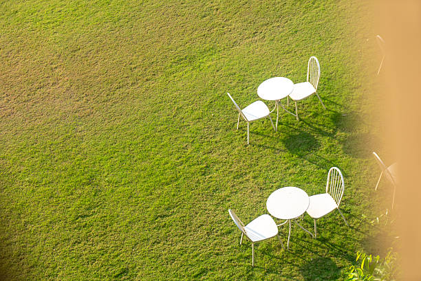 A serene outdoor scene featuring white tables and chairs on lush green grass under bright sunlight, creating a peaceful and inviting atmosphere for relaxation.