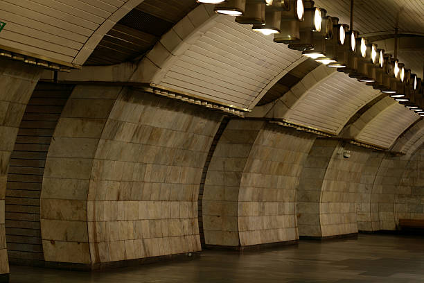 The interior of a vintage subway station features curved marble walls and a vaulted ceiling with rows of lights