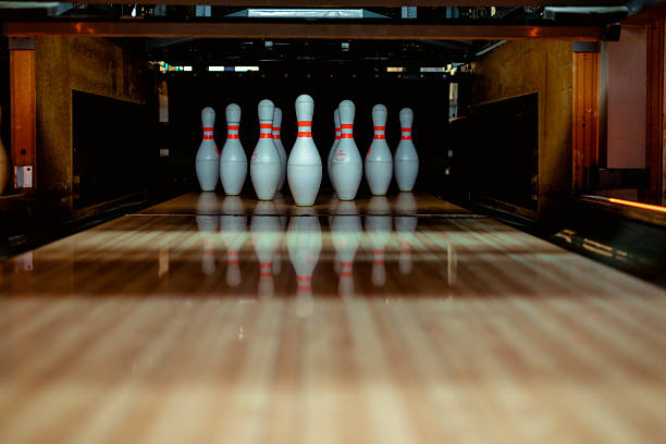 Close-up of white bowling pins arranged at end of polished wooden lane inside bowling club, ready for a strike. Perfect for sports, leisure, and recreation concepts.
