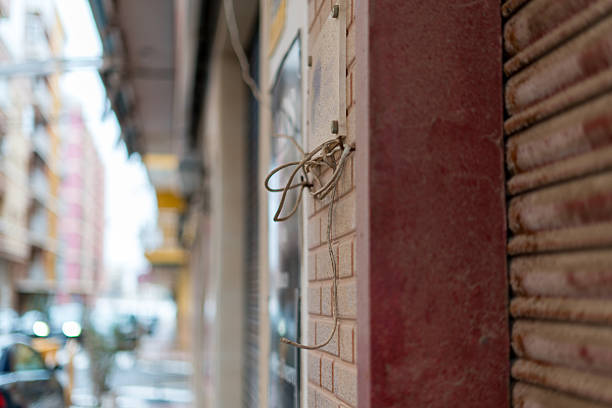 Close up of damaged exposed cables on exterior wall of urban building showing safety hazard and poor maintenance in city environment.