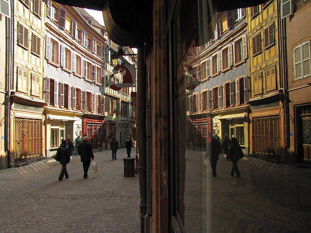 Rue des Marchands in Colmar, Alsace, lined with colorful half-timbered houses, boutique shops and reflective storefront glass, capturing the lively atmosphere of the historic old town, FR, 05 March 2011