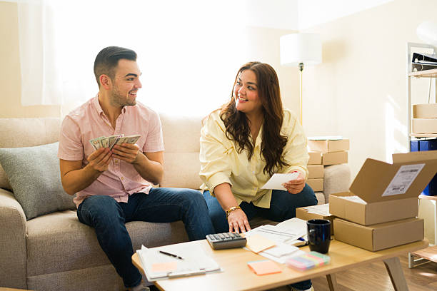 Happy couple counting cash and preparing shipping packages for an online store or successful entrepreneurial venture from their living room