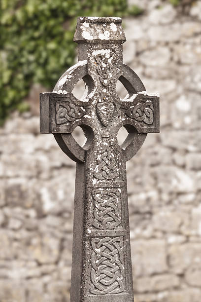 A close-up view captures the intricate details of a weathered Celtic high cross, featuring traditional knotwork patterns and natural aging from lichen growth, set against a blurred background.