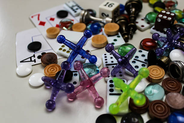 Assorted classic game pieces including jacks, dice, dominoes, marbles, go, and playing cards in a colorful pile. hobby and leisure background or banner