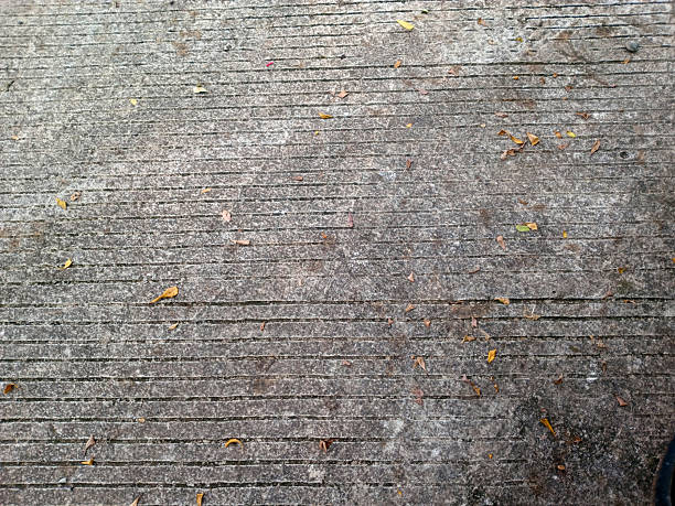Weathered concrete pavement with parallel grooves and scattered dry leaves, top down view, urban textured background with copy space.