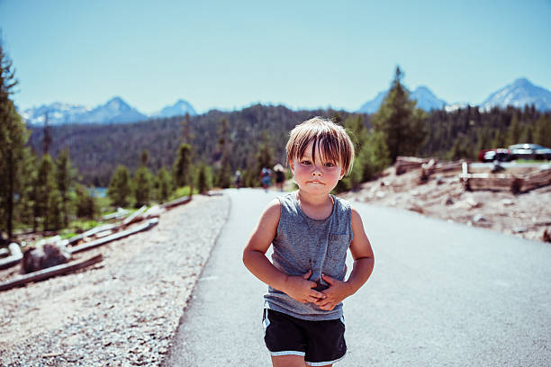 A young boy walks along a paved lakeside path with the Sawtooth Mountains rising behind him near Redfish Lake in Stanley, Idaho.