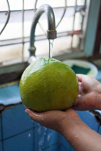 Close-Up of Washing Fresh Pomelo Under Running Tap Water