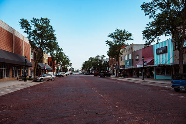 Parked cars line the brick-paved street in the charming historic Bricks District in downtown Kearney, Nebraska, featuring small businesses and storefronts at golden hour on a peaceful and beautiful summer evening.