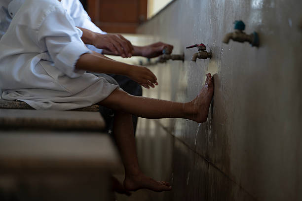 A father guides his young son through the steps of Wudu at a mosque's washing station, highlighting the importance of cleanliness and preparation in Islamic worship.