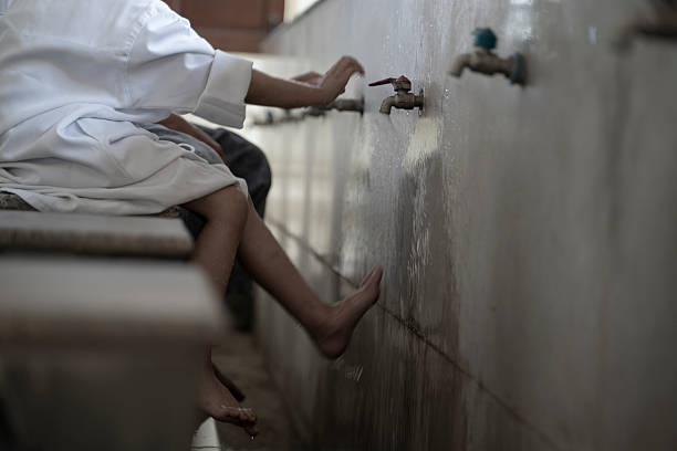 A father guides his young son through the steps of Wudu at a mosque's washing station, highlighting the importance of cleanliness and preparation in Islamic worship.