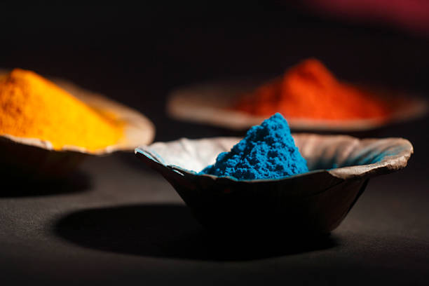 Close-up of vibrant blue Holi powder in a traditional leaf bowl with warm dramatic lighting and blurred colorful background.