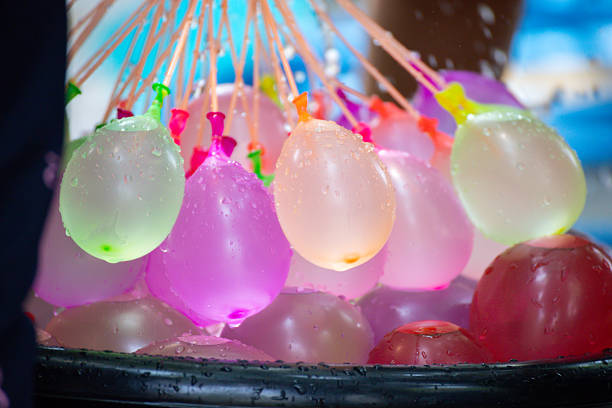 Three colorful water balloons bouncing back from a water-wetted glass plate amidst water splashes against a dark background.
