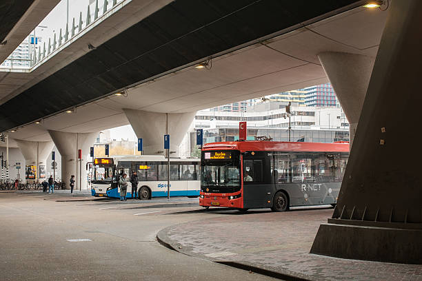Amsterdam, The Netherlands. February 19th, 2026: Color photograph of city buses waiting at the Amsterdam Bijlmer Arena bus station beneath an elevated roadway. The modern urban transport hub serves commuters and travelers, highlighting public transportation, infrastructure, and daily city mobility in the Netherlands.