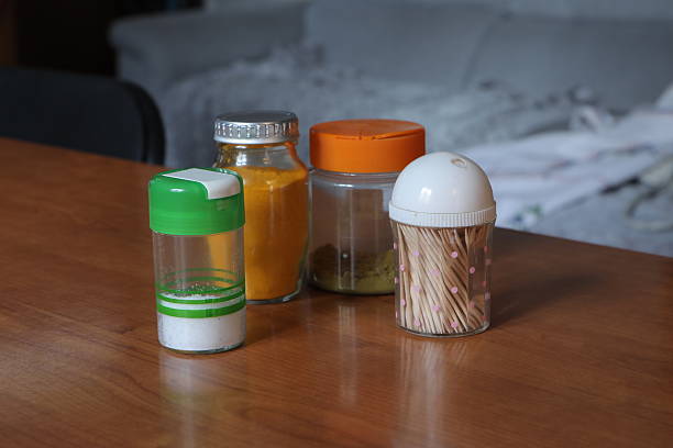 Salt shaker, spice jars, and toothpick holder sitting on a wooden kitchen table