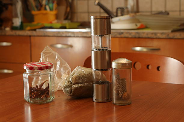 Assortment of dried spices and a pepper grinder sitting on a wooden kitchen table