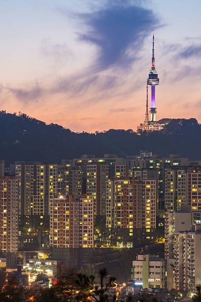 The iconic spire of Namsan Tower on the mountain at sunset overlooking the warmly lit highrise cityscape of central Seoul, South Korea’s vibrant capital city.