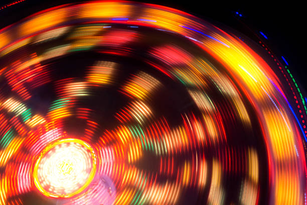 A Ferris wheel spins brilliantly in Avignon, France, its vibrant lights creating mesmerizing streaks against the night sky, showcasing dynamic energy and festive charm.