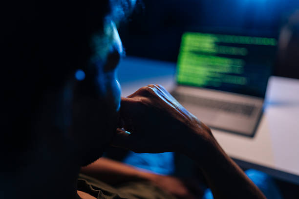 Pensive developer writing code late at night, working on programming software, debugging system issues, ensuring cyber security protection during dark room session, close-up back view stock photo