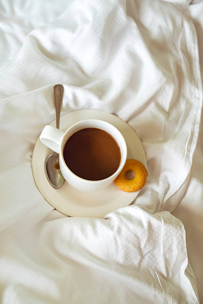Cup of coffee on white sheets in the bed