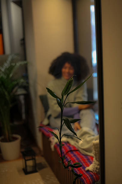 Woman smiling and relaxing on a cozy bench, reflecting in a mirror with a plant in foreground