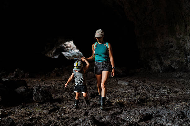 A mother holds her toddler’s hand while navigating uneven volcanic terrain inside Indian Tunnel at Craters of the Moon National Monument.