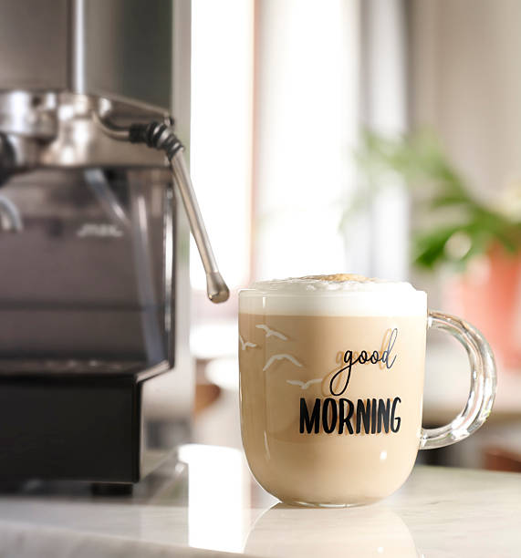 Coffee cup sits on a table next to an espresso machine in a kitchen during morning hours with natural light pouring in