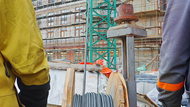 Workers near a building construction site with scaffolding, a crane, and a cable reel