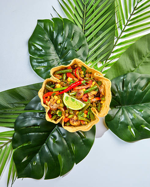 Fajitas in tortilla bowl with beef, cheese, corn and lettuce on faux monstera and palm leaf