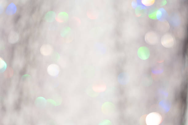 Soft, defocused bokeh lights with a silver, pastel glow create a magical, shimmering background. The image features a blend of muted hues—greens, blues, and pinks—interspersed across a predominantly white and silvery backdrop. This luminous, glittering texture is ideal for festive settings, such as weddings, Christmas, or other celebratory events, offering an abstract and decorative visual appeal.