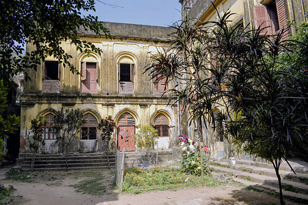 the yellow weathered facade of the inner courtyard at narajole rajbari palace featuring arched windows with wooden shutters and a small garden