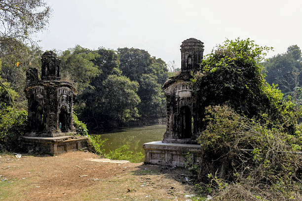 twin weathered masonry shrines with ribbed domes stand at the edge of a reservoir, flanked by overgrown greenery and wild shrubs