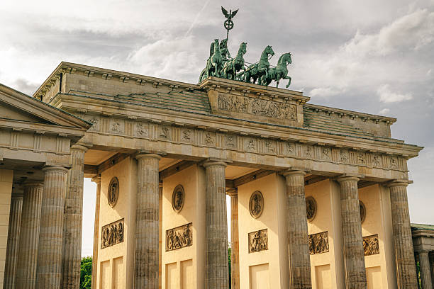 Brandenburg Gate in Berlin illuminated by warm late-afternoon light, showcasing its neoclassical columns, Quadriga sculpture and carved reliefs. A historic German landmark symbolizing culture, tourism and European architectural heritage.