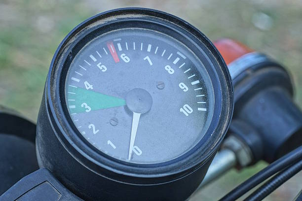 one black round plastic tachometer speedometer on the dashboard of an old motorcycle on a summer street