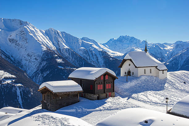 Chapel Maria in Snow (Kapelle zum Schnee) with two old chalets - the landmark architecture in the Swiss alps village Bettmeralp in Canton Vaud. It is one of the famous winter sport resort.