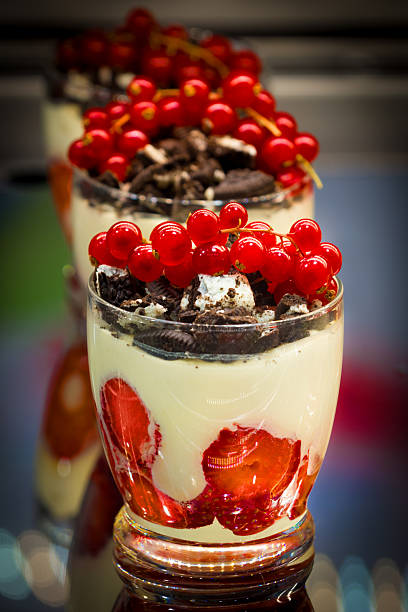Vanilla custard topped with strawberries, red currants, and biscuit pieces in the display window of a bakery.