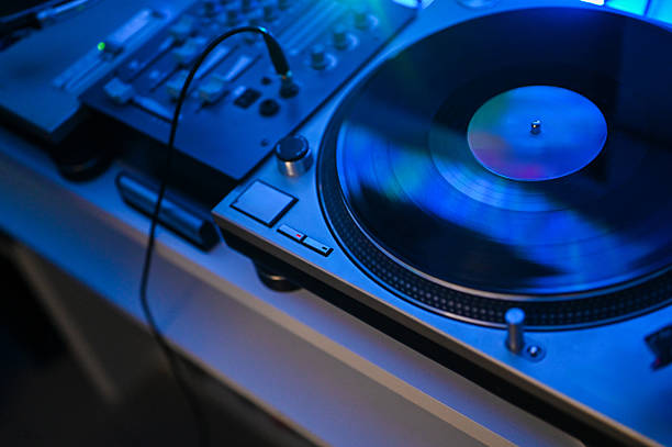Turntable spinning a vinyl record, creating music with a mixer under blue light