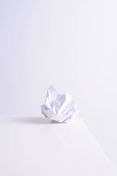 A crumpled paper ball sits on a flat white surface. It is the only object in the area, with a plain background.