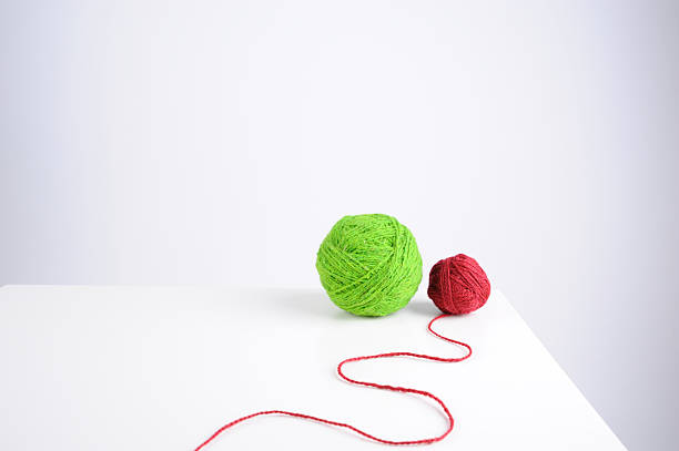 A large green ball of yarn and a smaller red ball sit on a white table. A red string connects the two yarn balls, creating a simple yet clear display.