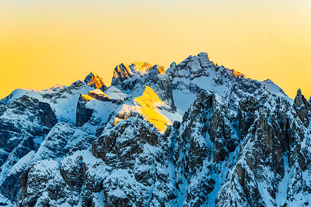 Snow-covered alpine cliffs and rugged mountain peaks illuminated by warm sunset light in a high-altitude winter landscape of the Dolomites in northern Italy.
