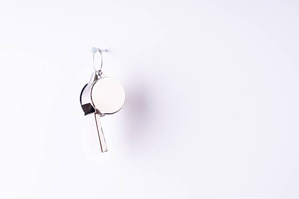 A silver key and whistle hanging on a wall. The key is silver and has a hole in it