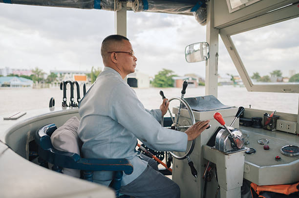 Side view of ferry driver managing vessel controls while navigating across an urban river. Real working environment representing transportation services, professional responsibility, and waterway commuting systems. Strong relevance for infrastructure, travel industry, workforce lifestyle, and public transport narratives.