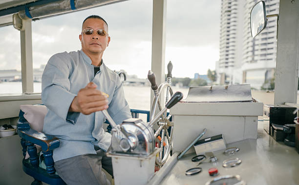 Boat captain operating steering controls inside passenger ferry navigating a busy city river route. Authentic public transportation scene emphasizing maritime profession, navigation responsibility, and daily commuting infrastructure. Ideal for transportation industry visuals, logistics concepts, travel documentary themes, and urban mobility storytelling.